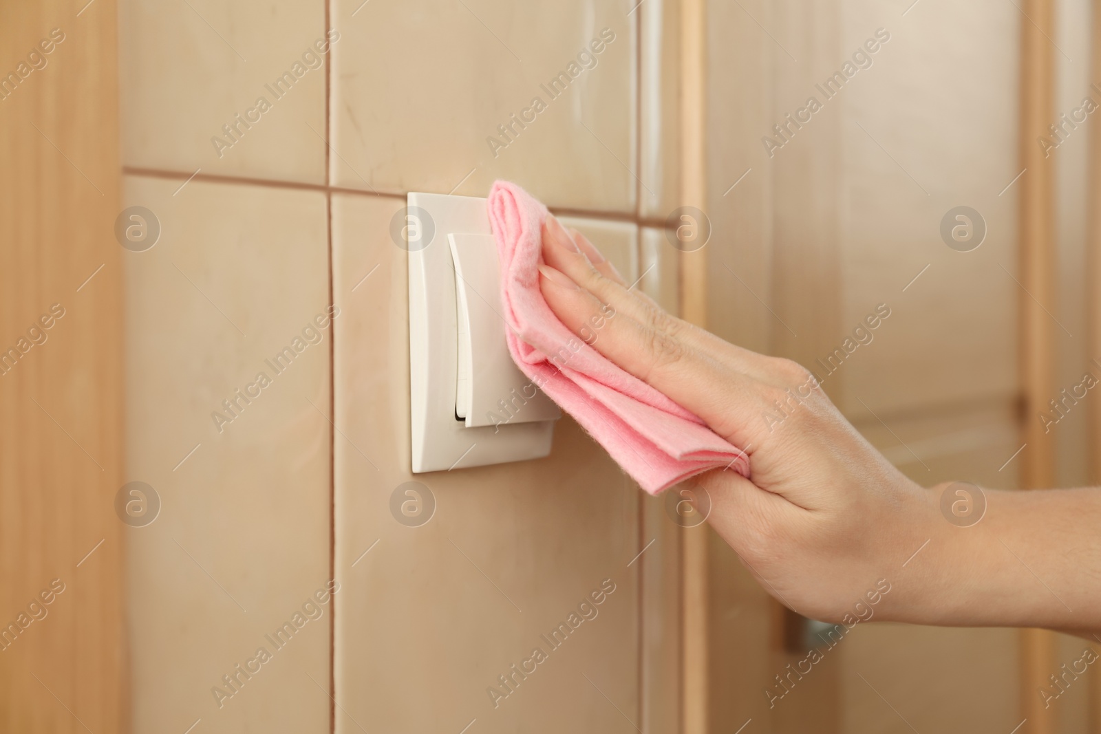 Photo of Woman cleaning light switch with rag indoors, closeup