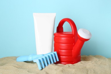 Photo of Suntan product and plastic beach toys on sand against light blue background