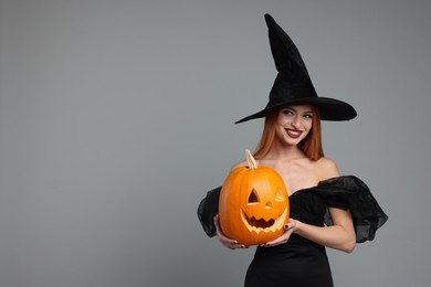 Photo of Happy young woman in scary witch costume with carved pumpkin on light grey background, space for text. Halloween celebration