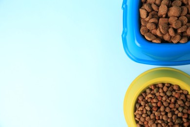 Photo of Dry pet food in feeding bowls on light blue background, flat lay. Space for text