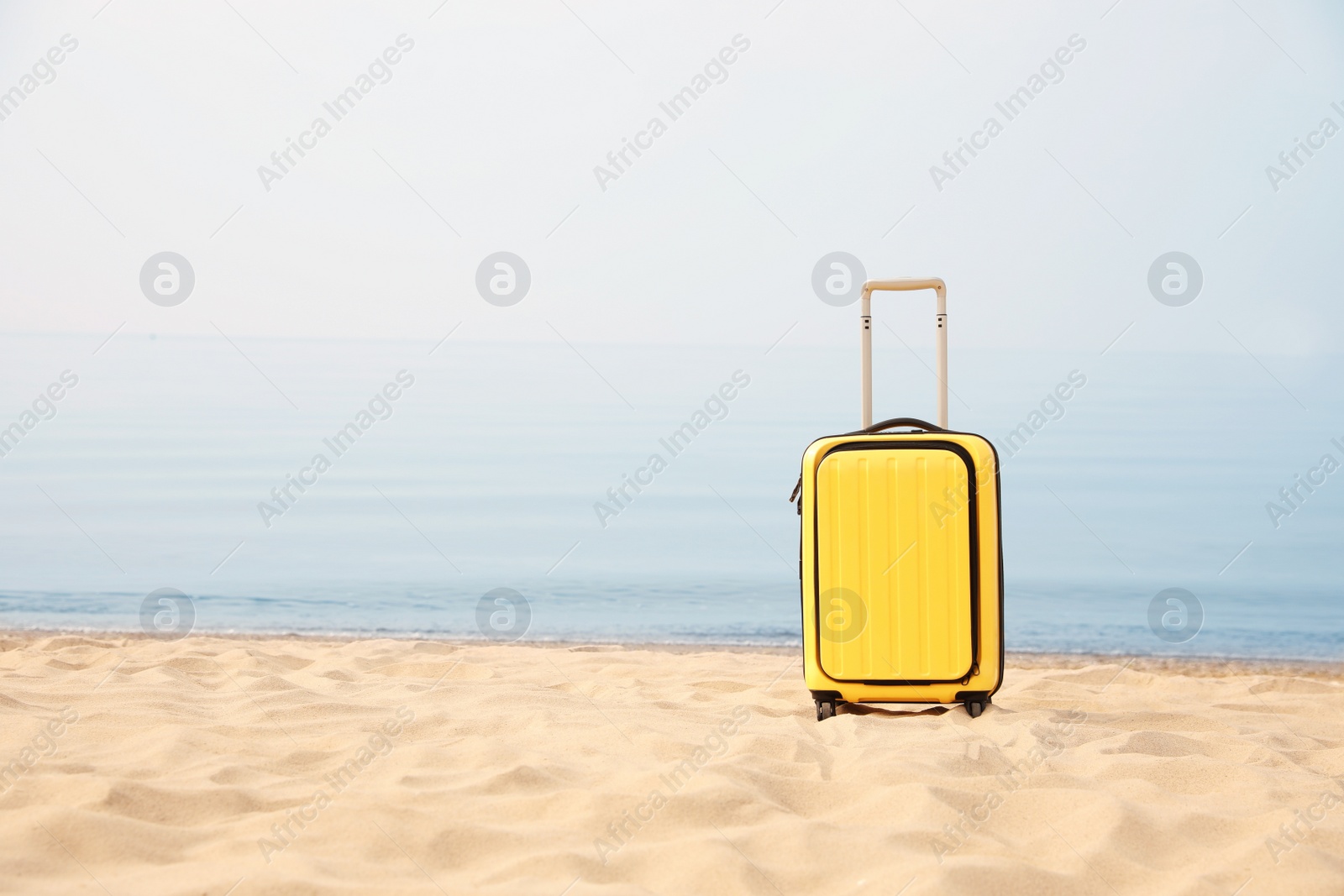 Photo of Yellow suitcase on sandy beach, space for text