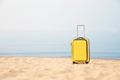 Yellow suitcase on sandy beach, space for text