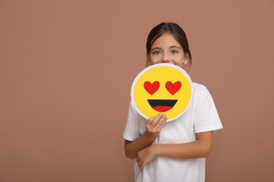 Photo of Little girl holding face with heart eyes emoji on pale pink background, space for text