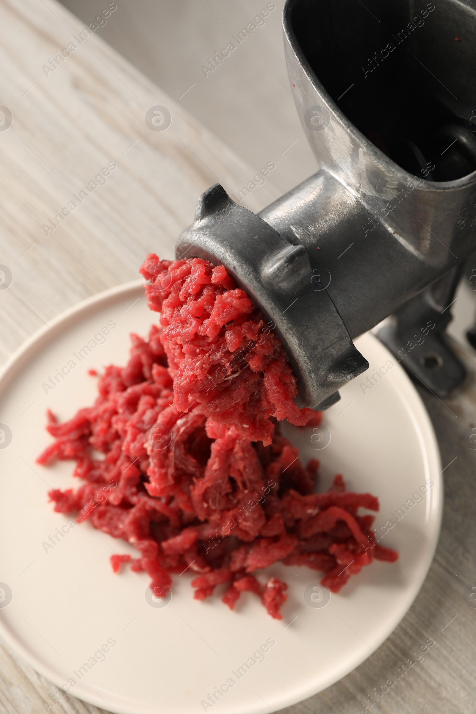 Photo of Metal meat grinder with beef mince on light wooden table, above view