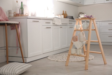 Photo of Decorative ladder with different dishware and field flowers bouquet in stylish kitchen. Idea for interior design