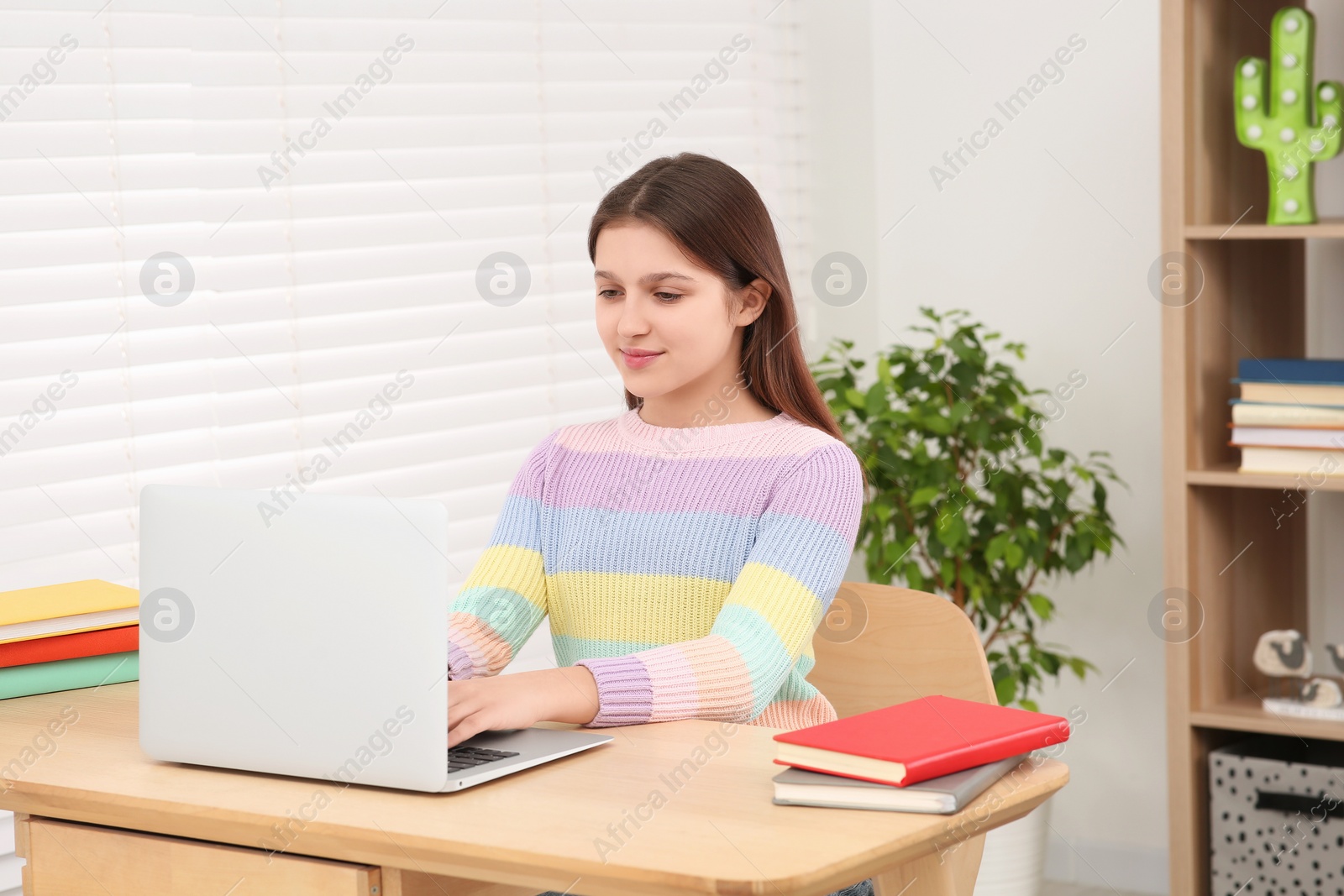 Photo of Cute girl using laptop at desk in room. Home workplace