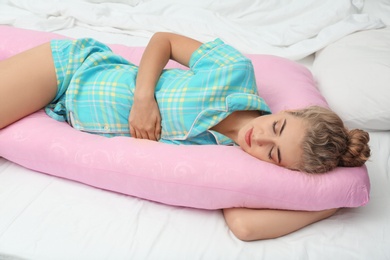 Photo of Beautiful pregnant woman sleeping with maternity pillow on bed at home