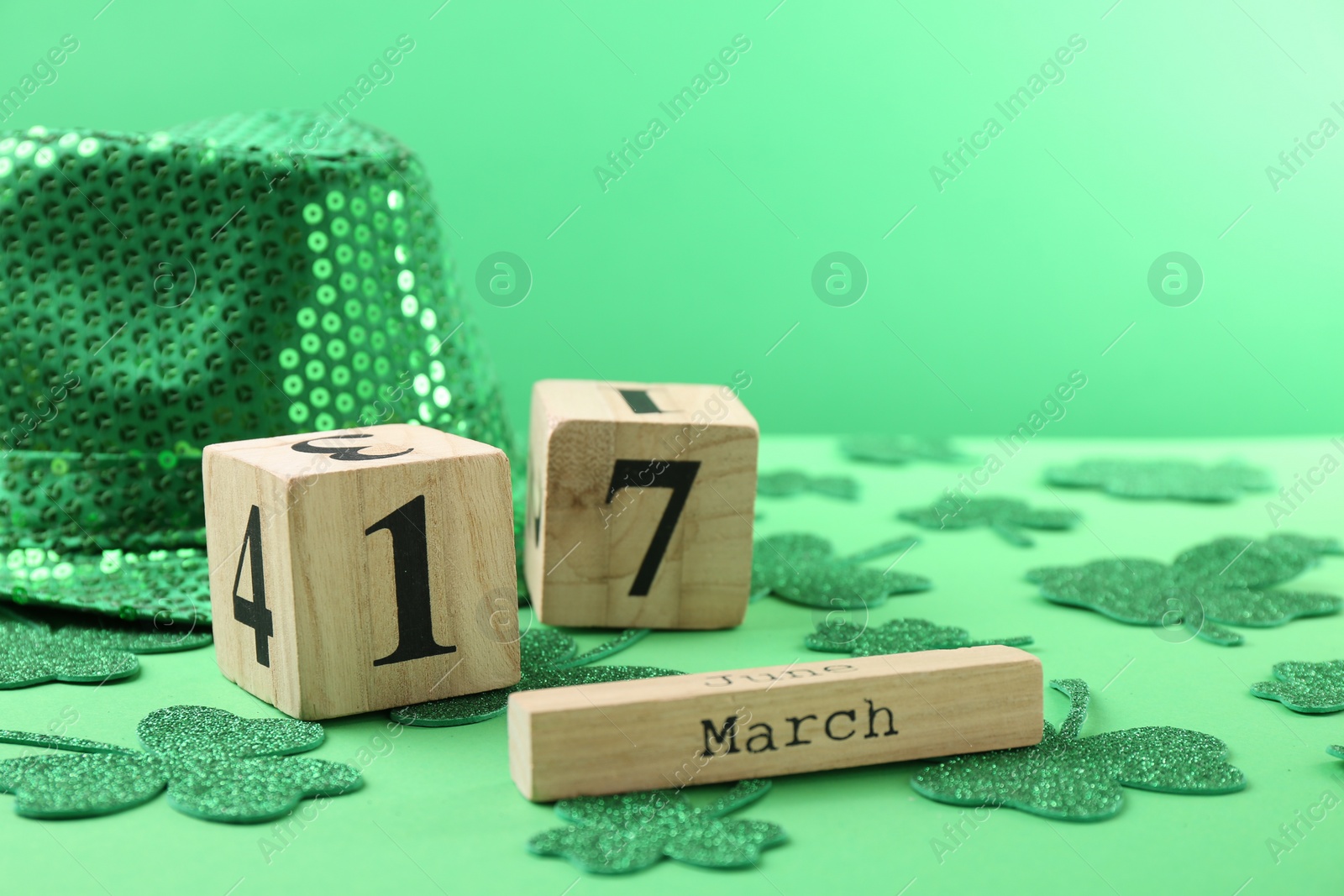 Photo of St. Patrick's day - 17th of March. Wooden block calendar, leprechaun hat and decorative clover leaves on green background. Space for text