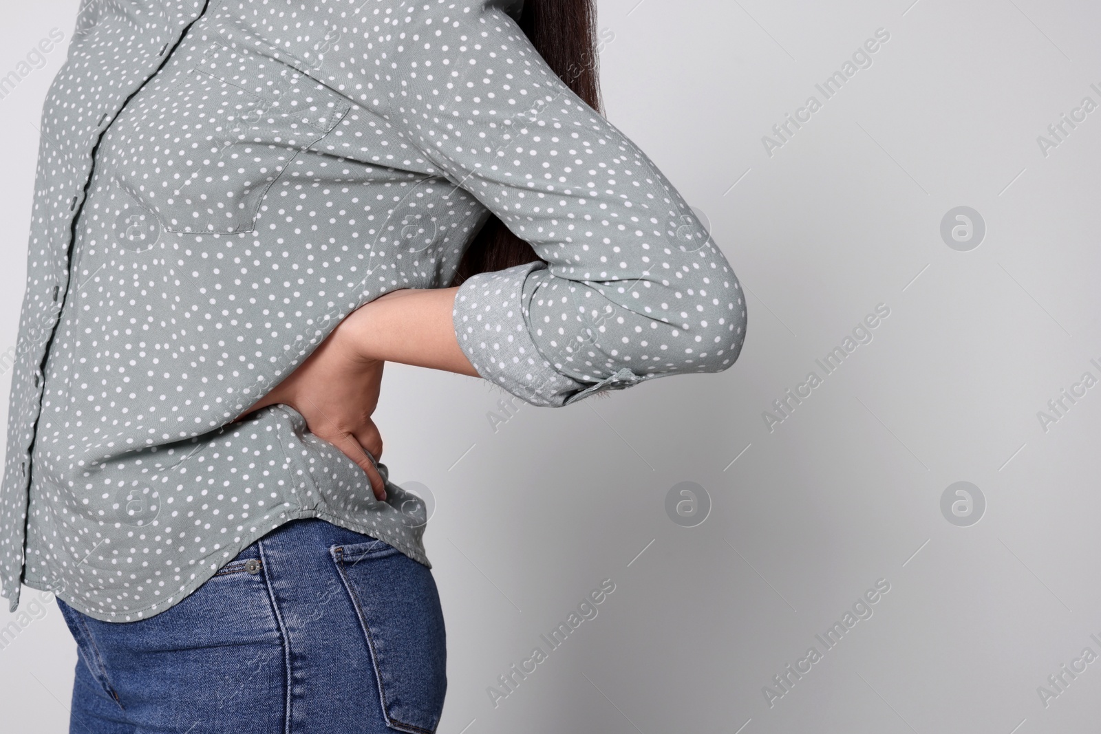 Photo of Young woman suffering from pain in back on light grey background, closeup with space for text. Arthritis symptoms