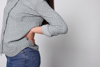 Photo of Young woman suffering from pain in back on light grey background, closeup with space for text. Arthritis symptoms