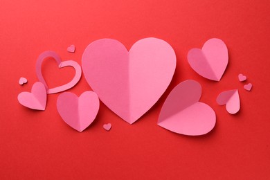 Photo of Pink paper hearts on red background, flat lay