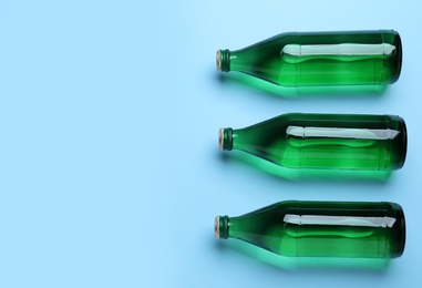 Glass bottles with water on light blue background, flat lay. Space for text