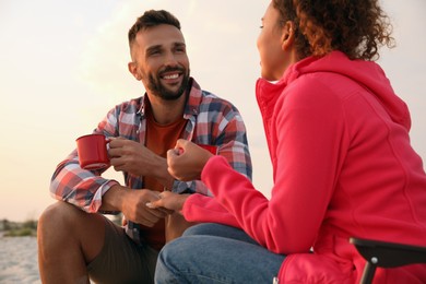 Lovely couple with cups of hot drinks outdoors. Beach camping