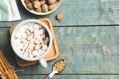 Photo of Hot drink with marshmallows and nutmeg powder on blue wooden table, flat lay. Space for text