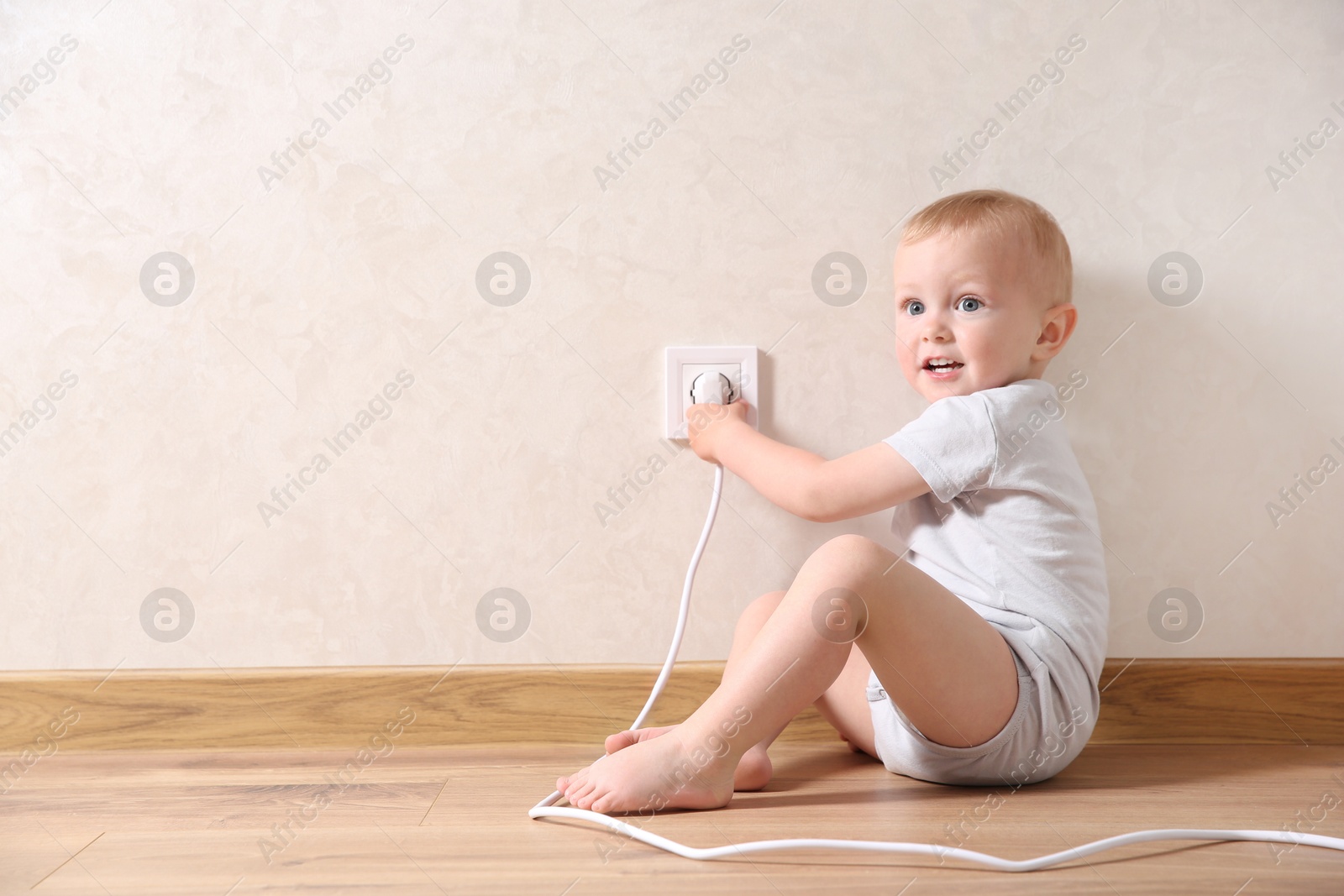 Photo of Little child playing with electrical socket and plug indoors, space for text. Dangerous situation