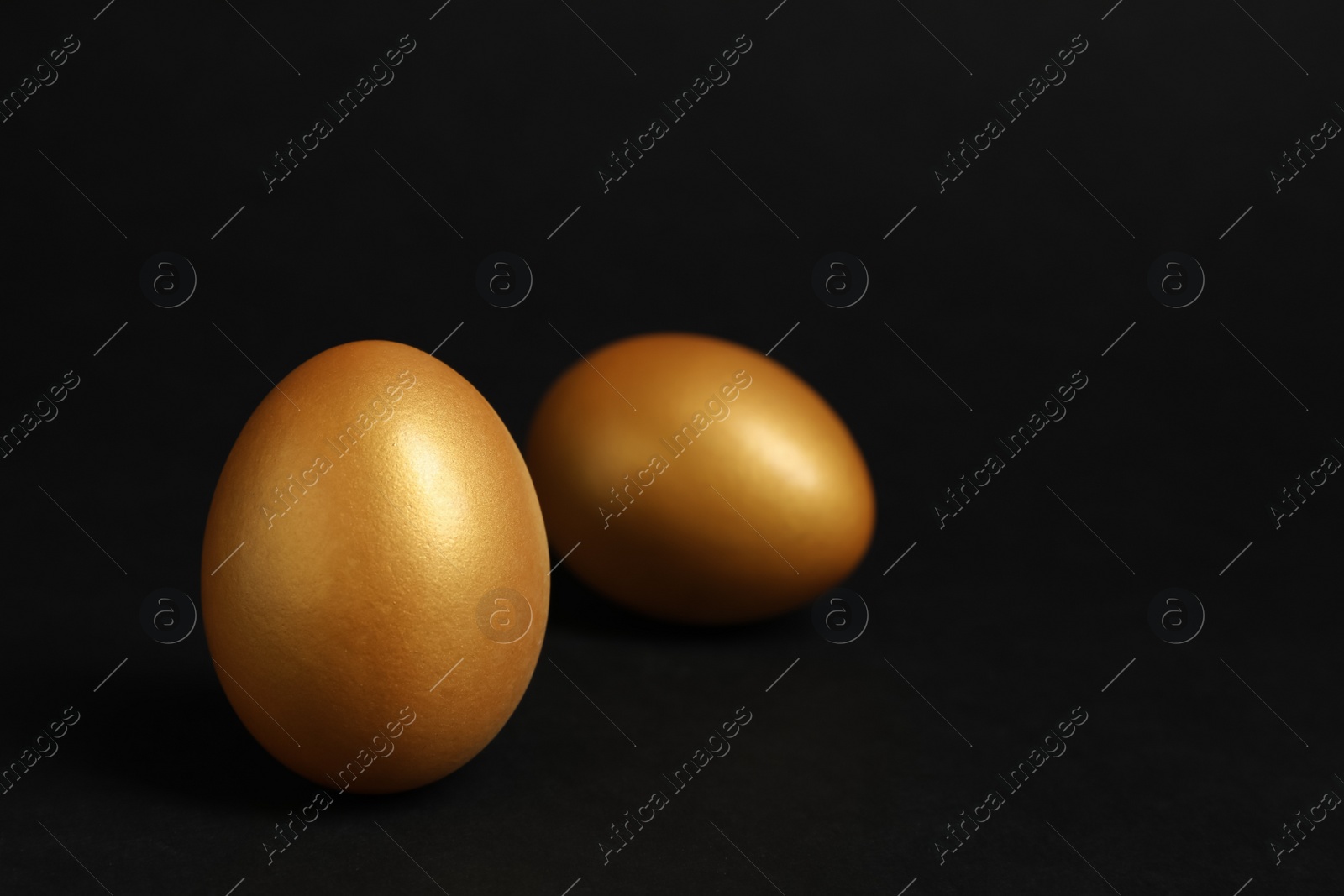 Photo of Shiny golden eggs on black background, space for text