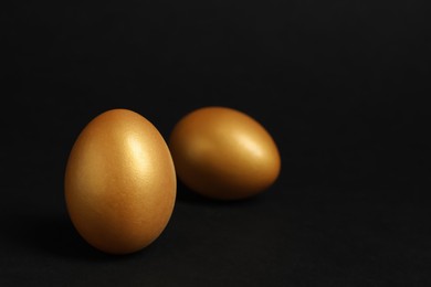 Shiny golden eggs on black background, space for text