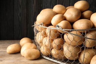 Photo of Raw fresh organic potatoes on wooden table against dark background, closeup. Space for text