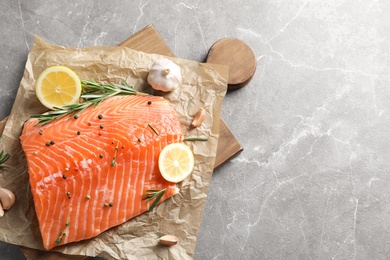 Photo of Wooden board with raw salmon and ingredients for marinade on grey background, top view