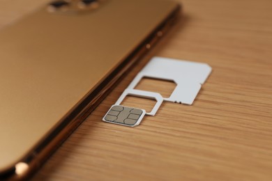 Photo of SIM cards and mobile phone on wooden table, closeup