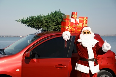 Photo of Authentic Santa Claus near car with presents and fir tree on roof outdoors