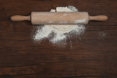 Photo of Flour and rolling pin on wooden table, top view. Space for text