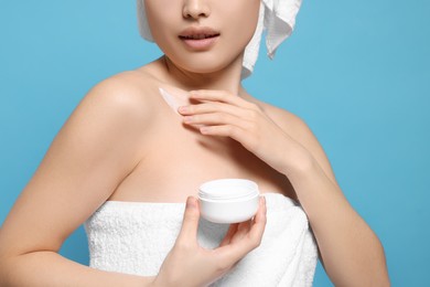 Young woman with jar of body cream on light blue background, closeup