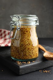 Whole grain mustard in jar and dry seeds on black table