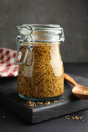 Photo of Whole grain mustard in jar and dry seeds on black table