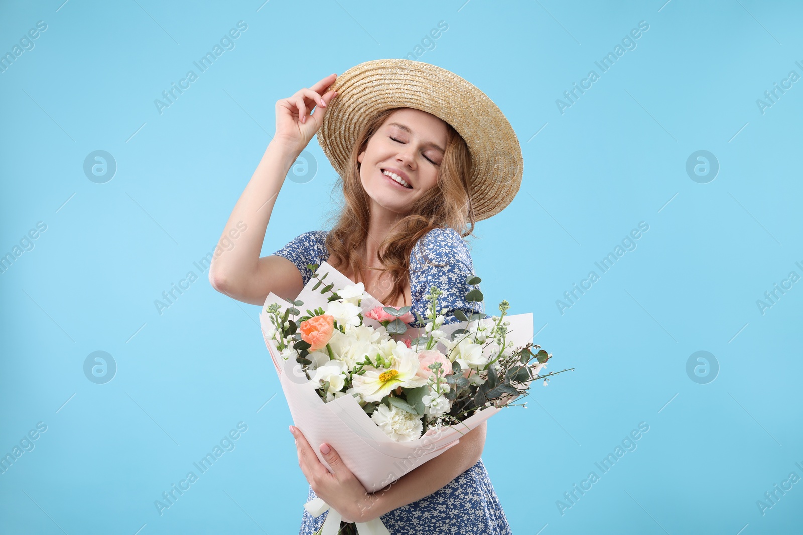 Photo of Beautiful woman in straw hat with bouquet of flowers on light blue background