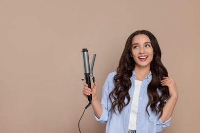 Photo of Happy woman with curling hair iron on beige background. Space for text