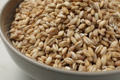 Photo of Dry pearl barley in bowl on white table, closeup