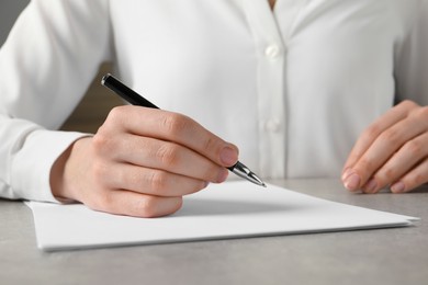 Woman with pen and paper sheets at grey table, closeup
