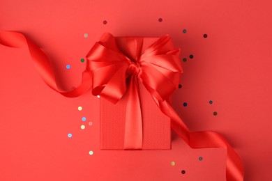 Beautiful gift box with bow and confetti on red background, top view