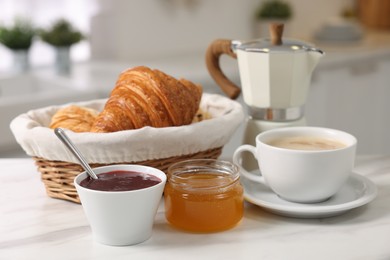 Photo of Breakfast served in kitchen. Fresh croissants, jam, honey and coffee on white table