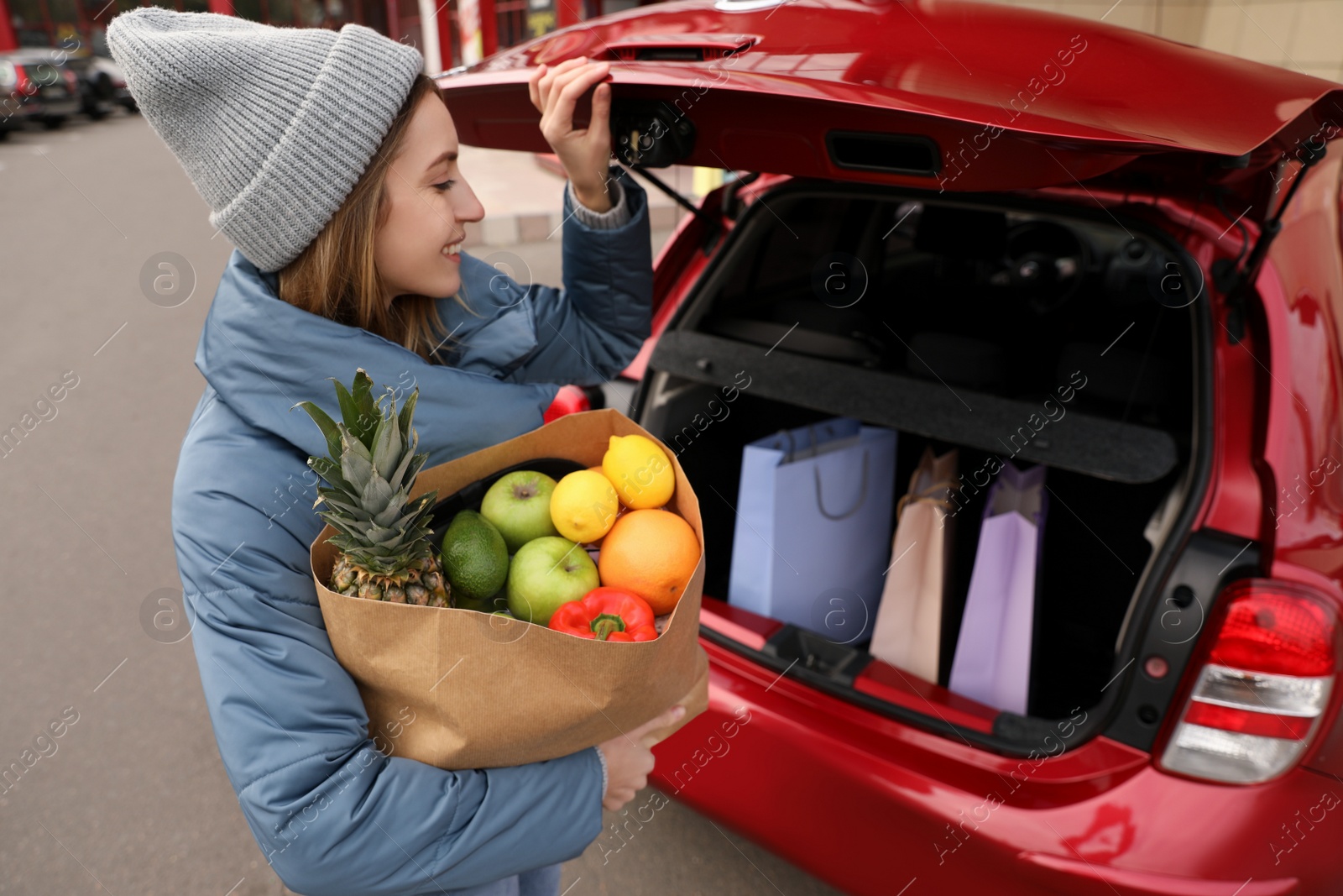 Photo of Young woman with bag of groceries near her car outdoors