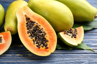 Photo of Fresh ripe papaya fruits with green leaves on wooden table, closeup