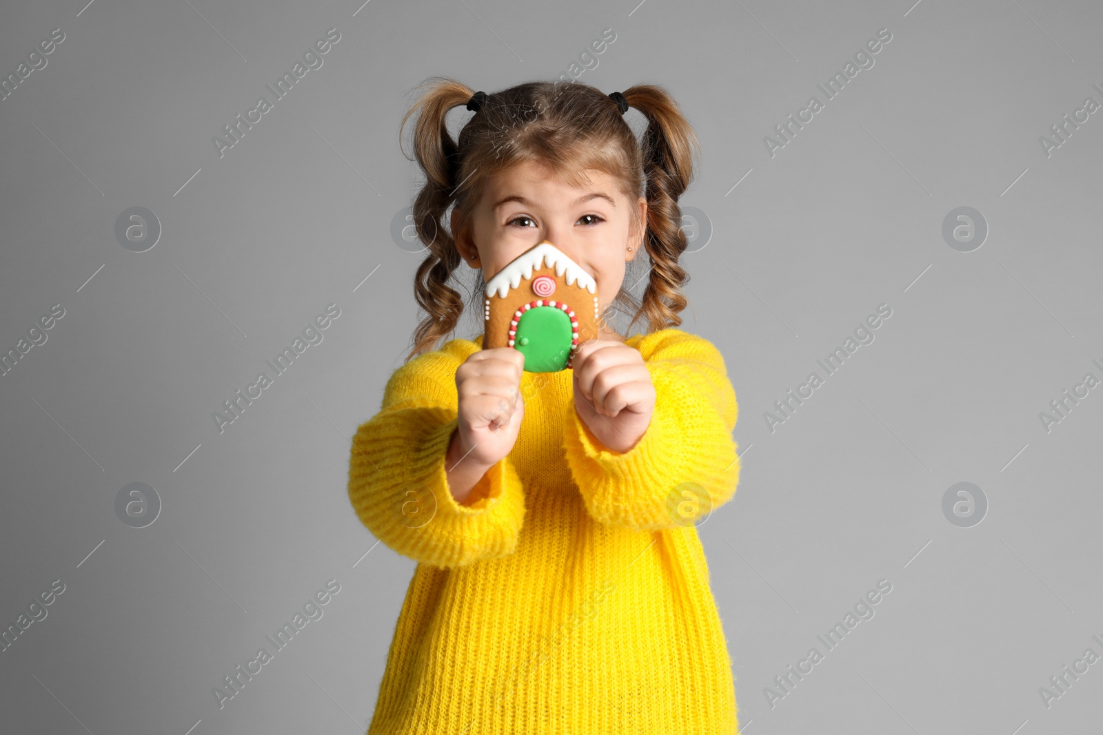 Photo of Cute little girl with Christmas gingerbread cookie on light grey background