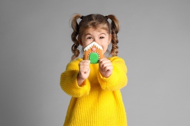 Cute little girl with Christmas gingerbread cookie on light grey background