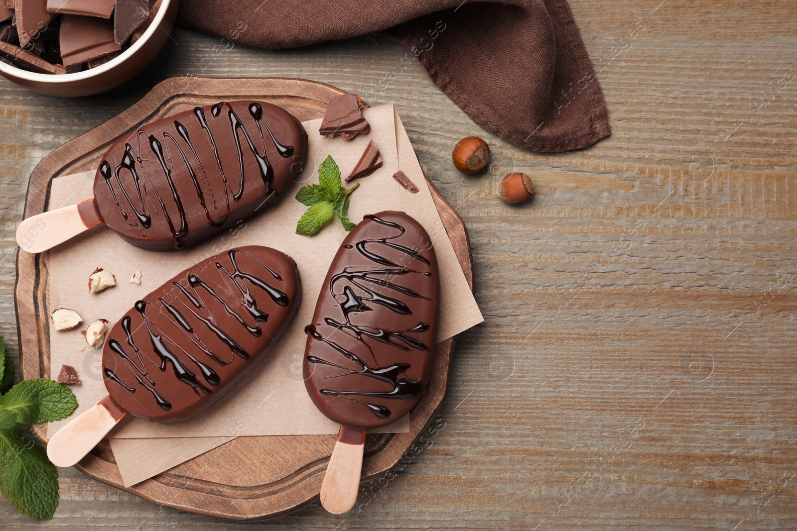 Photo of Delicious glazed ice cream bars, nuts and mint on wooden table, flat lay. Space for text