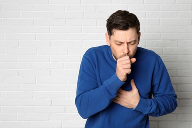 Man suffering from cough near brick wall. Space for text