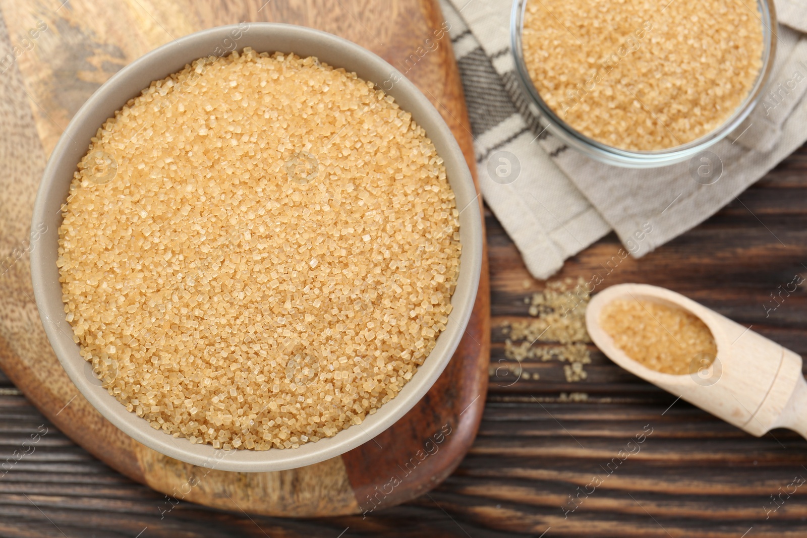 Photo of Brown sugar in bowls and scoop on wooden table, flat lay