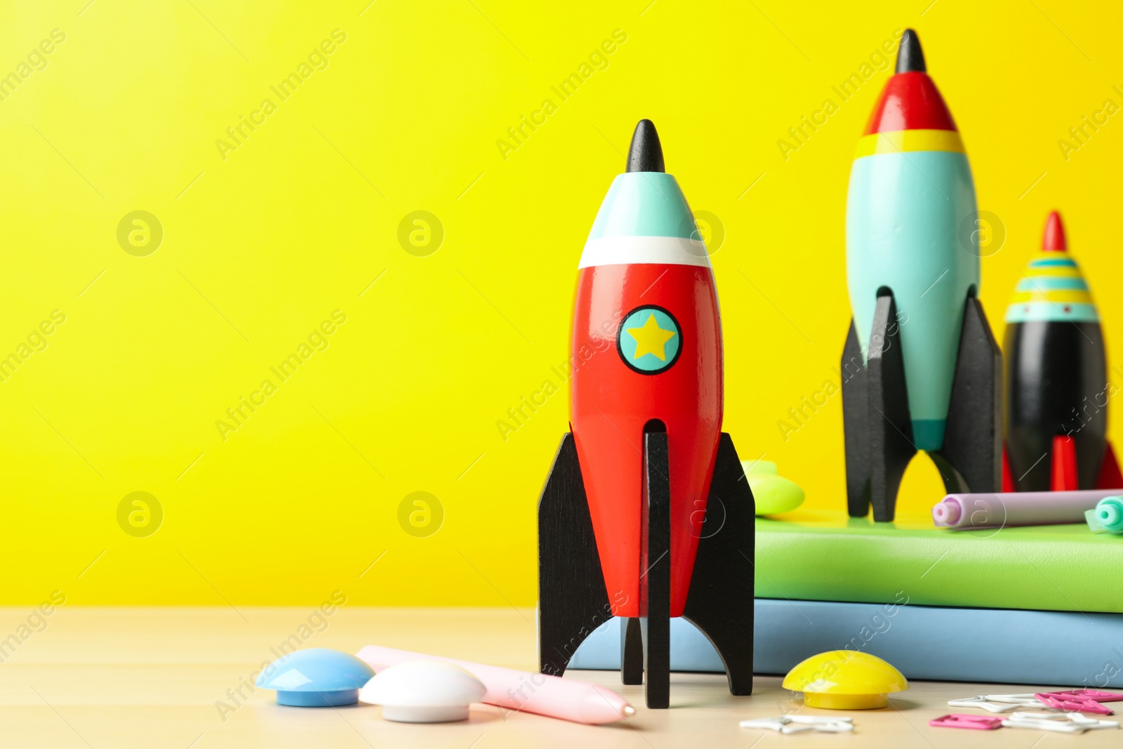 Photo of Bright toy rockets and school supplies on wooden table. Space for text