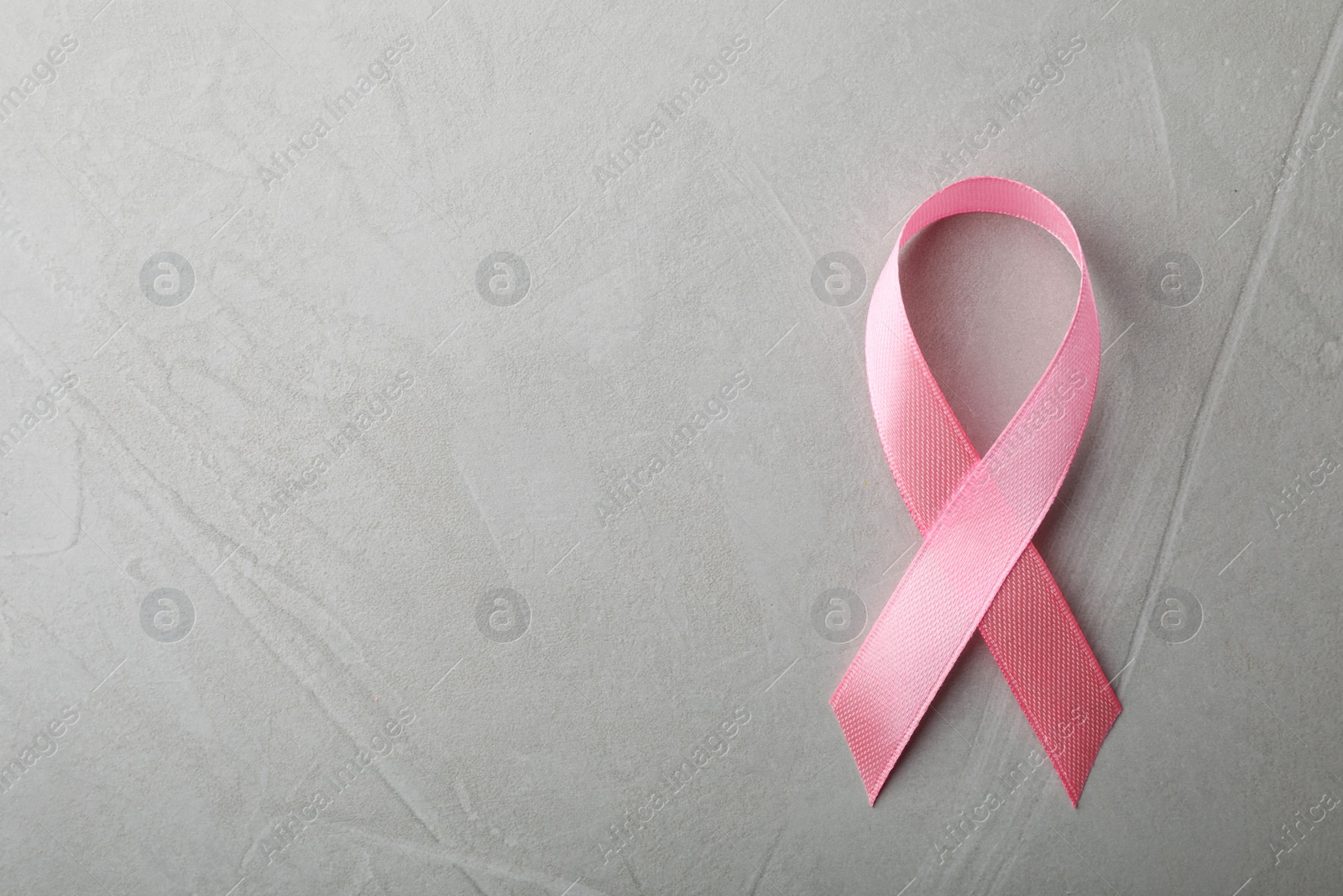 Photo of Pink ribbon on grey background, top view with space for text. Breast cancer awareness concept