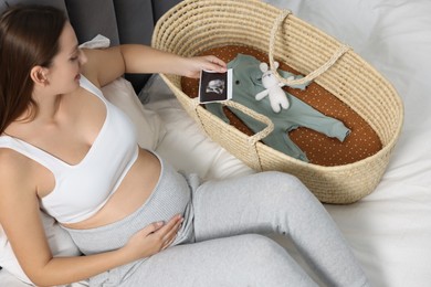 Photo of Pregnant woman with ultrasound picture of baby and basket on bed, above view