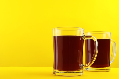 Photo of Delicious homemade kvass in glass mugs on yellow background. Space for text