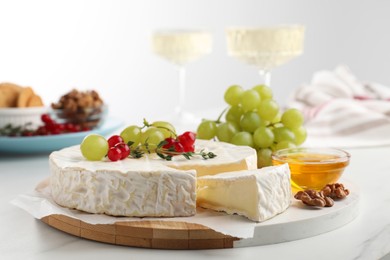 Photo of Brie cheese served with honey and berries on white table