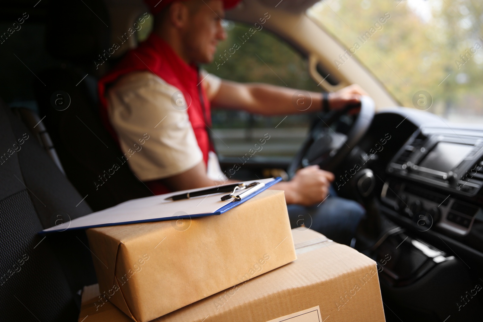 Photo of Courier driving delivery van, focus on parcels and clipboard