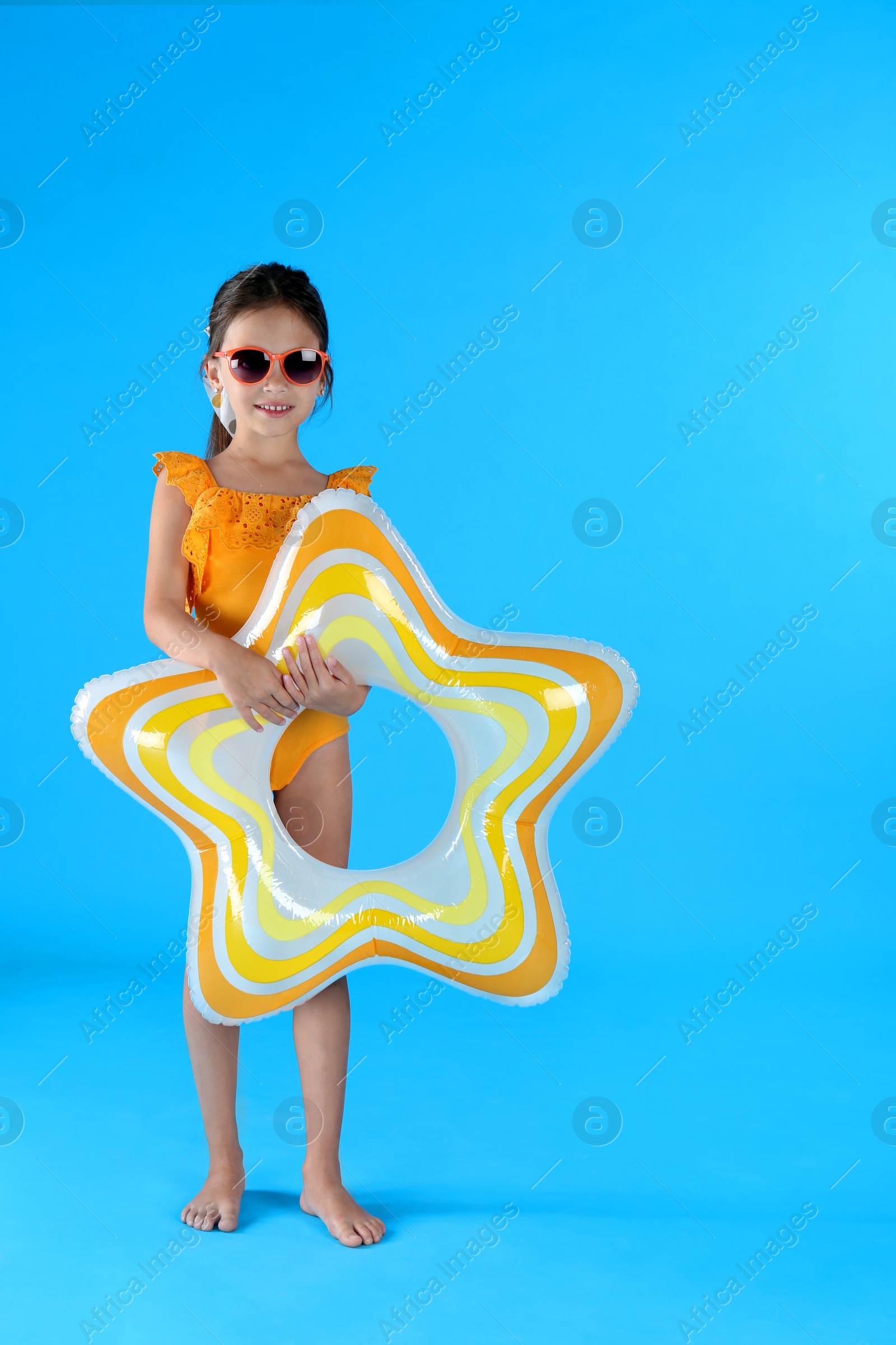 Photo of Cute little child in beachwear with inflatable ring on light blue background