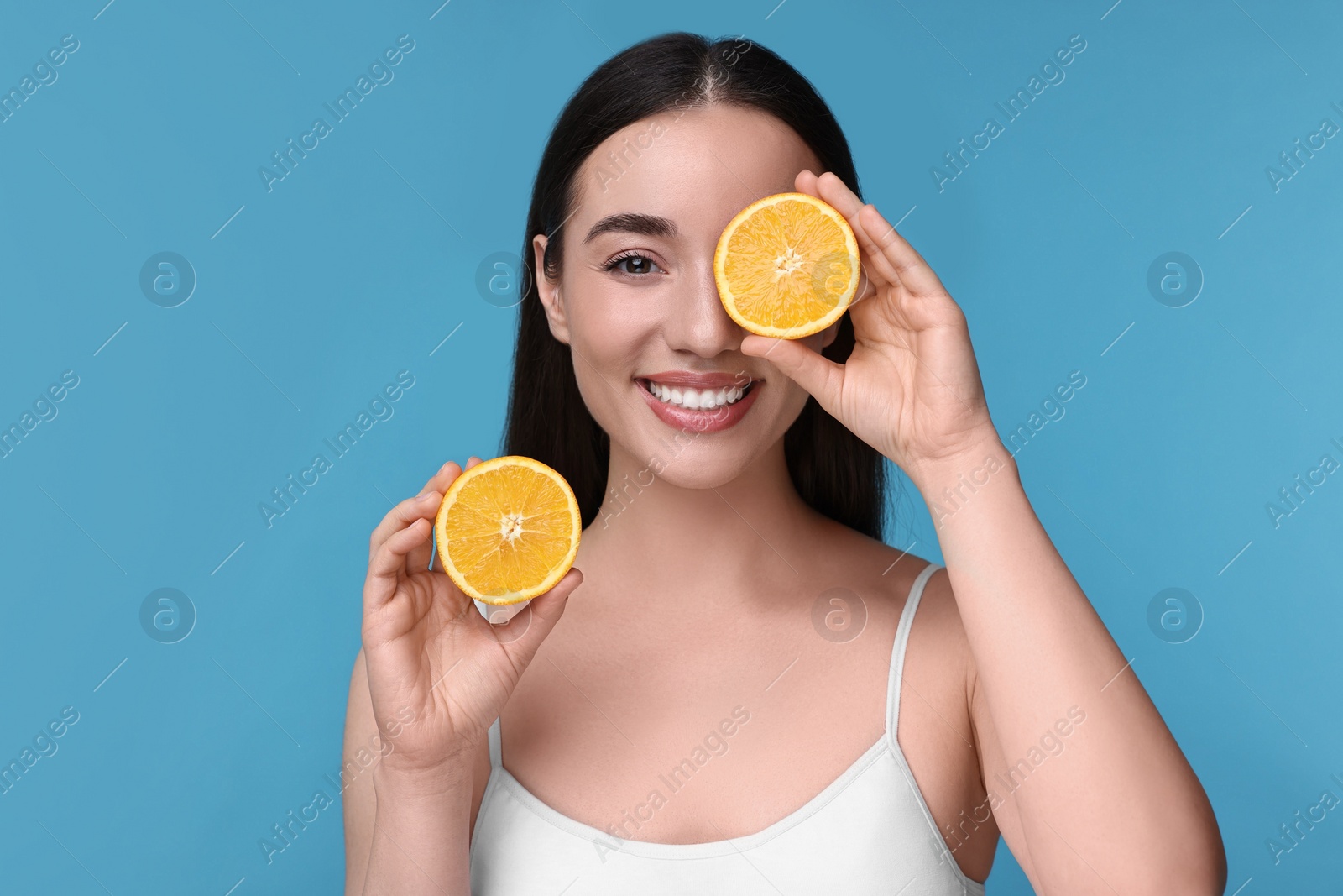 Photo of Beautiful young woman with pieces of orange on light blue background